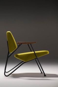 a yellow chair sitting next to a wooden table on top of a gray floor in front of a black wall