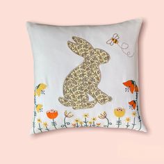 a white pillow with an image of a rabbit sitting on top of flowers and butterflies