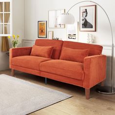 an orange couch sitting on top of a wooden floor next to a lamp and pictures