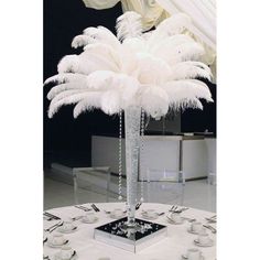 a white table topped with a tall vase filled with feathers and silver place settings on top of it