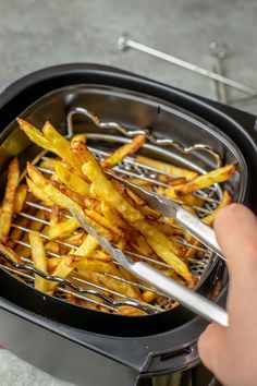 french fries being cooked in an air fryer with tongs on the side,