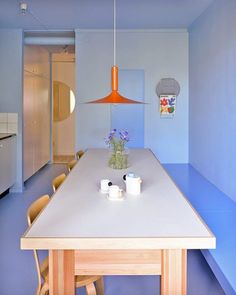 a kitchen with blue walls and white countertops, wooden chairs and a table in the center