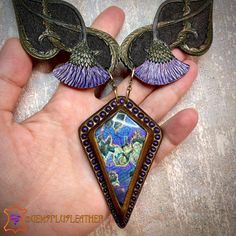 a close up of a person's hand holding a piece of jewelry with wings on it