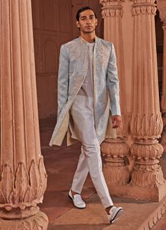 Presenting the Aqua Blue Applique Sherwani Set, a masterpiece that exudes timeless charm and sophistication. Crafted from luxurious jacquard silk, this aqua blue sherwani showcases a stunning tissue applique technique, beautifully complemented by intricate zardozi and dabka embroidery. The design features large, graceful leaf-like motifs and delicate floral details, meticulously placed to create a visually striking ensemble. Paired with a front open white kurta, adorned with fine detailing on the placket, adding an extra touch of elegance. Completed with complementary white pants, this outfit is perfect for those who appreciate a seamless blend of traditional craftsmanship and modern style. Ideal for Mehndi, Sangeet, or as wedding guest attire, this sherwani set ensures you make a lasting Blue Sherwani With Intricate Embroidery For Ceremonial Occasion, Blue Sherwani With Intricate Embroidery For Ceremonial Wear, Blue Embroidered Sherwani For Reception, Blue Sherwani With Intricate Embroidery For Transitional Season, Designer Embroidered Blue Sherwani, Light Blue Traditional Formal Sets, Traditional Light Blue Formal Sets, Blue Sherwani With Naqshi And Traditional Drape, Blue Sherwani With Naqshi In Traditional Drape