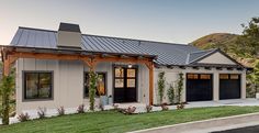 a white house with black garage doors on the front and side of it, surrounded by greenery