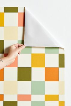 a person's hand holding an envelope over a colorful checkered pattern wallpaper