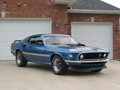 a blue mustang parked in front of a brick house