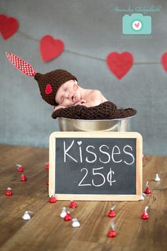 a baby in a bucket with a sign that says kisses 25 cents on it and hearts floating around