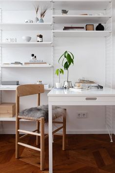 a white desk and chair in a room with shelving on the wall behind it