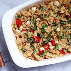 a casserole dish filled with pasta, tomatoes and spinach on a marble surface