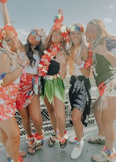 four beautiful young women standing next to each other in front of a fence with leis