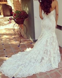 a woman in a wedding dress leaning against a wall with her back to the camera