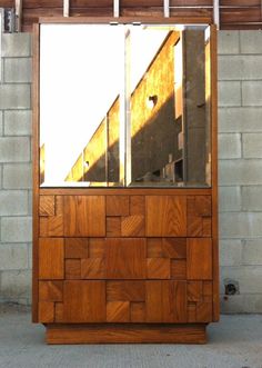 a large wooden cabinet sitting in front of a brick wall with two mirrors on it's sides