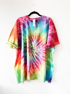 a colorful tie - dyed shirt hangs on a hanger in front of a white wall