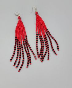 red and black beaded earrings with long tassels hanging from hooks on grey background