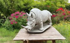 a rhinoceros statue on top of a wooden table in the middle of a garden