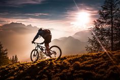 a person riding a bike on top of a hill with the sun in the background