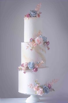 a three tiered white wedding cake with pink and blue flowers