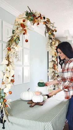 a woman decorating a table with pumpkins and greenery