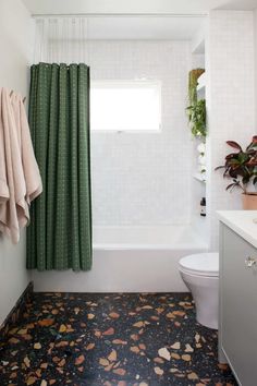 a bathroom with a toilet, tub and shower curtain that has green leaves on the floor