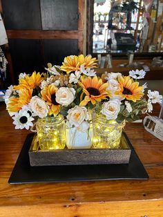 sunflowers and roses are in mason jars on a wooden table with string lights