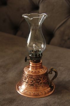 an old fashioned glass and brass oil lamp on a couch with a brown sofa in the background