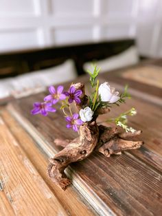 purple and white flowers are placed in a driftwood vase on a wooden table top