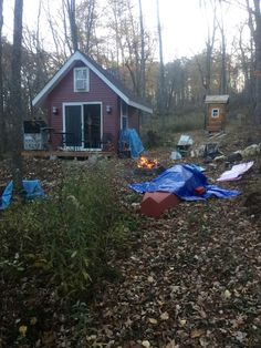 there are many tents set up in the woods near a small red house with a blue tarp on it