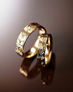 two gold wedding rings sitting next to each other on a black surface with reflections in the background