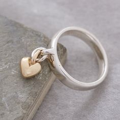 Add charm to your jewellery collection with our exquisite and unique solid silver ring, adorned with a delicate sweetheart recycled gold heart charm that gracefully sways with your every move. This everyday yet extraordinary ring is destined to spark conversations and become a cherished part of your personal style. Craftsmanship: Meticulously crafted using traditional lost wax casting techniques, our solid sterling silver rings are designed for both aesthetics and comfort. The ring features a robust and enduring loop on the front, while its generous band shape prioritizes comfort, durability, and contemporary elegance. The dangling heart charm is crafted from your choice of either recycled solid rose gold, or recycled solid yellow gold, with a beautifully rounded, organic shape. Quality As Ring With Charms, Charm Rings Dangle, Chunky Silver Rings, Gold Heart Ring, Charm Ring, Unusual Rings, Silver Signet Ring, Rose Gold Heart, Designer Fashion Jewelry