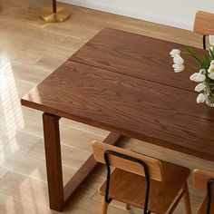 a wooden table with two chairs next to it and a vase filled with white flowers