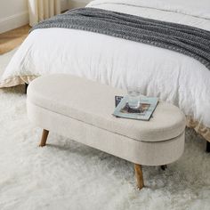 a bed with a white blanket and a foot stool in front of it on a shaggy rug