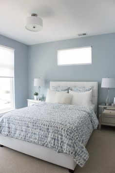 a bedroom with blue walls, white bedding and two lamps on either side of the bed