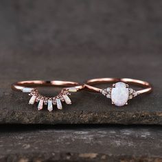 two gold rings with opal and diamond accents on top of a stone slab in the woods