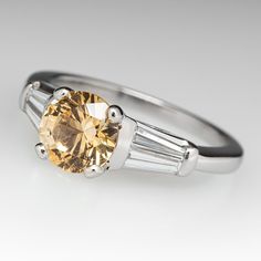 This incredible sapphire engagement ring features a 1.43 carat yellow sapphire with Montana origin that we sourced and set in a vintage platinum diamond mounting. The shoulders of the ring are each accented with two (2), channel set, tapered baguette cut diamonds. The ring measures 6.6mm at the top, rises 7.7mm above the finger, tapering to 1.7mm wide and 1.4mm thick at the base of the shank. The ring is currently a size 4.75 and we offer complimentary resizing to fit. Montana Sapphire Engagement, Montana Sapphire Engagement Ring, Montana Sapphire, Sapphire Engagement Ring, Baguette Cut Diamond, Ruby Jewelry, July Birthstone, Channel Set, Baguette Cut