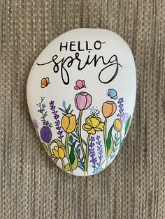 a painted rock that says hello spring with flowers and butterflies on it sitting on a carpet