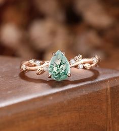 a close up of a ring on top of a wooden surface with leaves and an oval shaped green stone