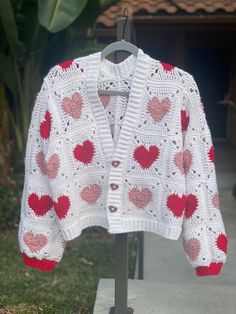 a crocheted cardigan with hearts on it is hanging from a rack outside