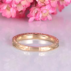 a close up of a wedding ring on a pink background with flowers in the background