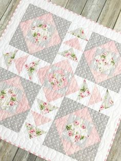 a pink and gray quilted table topper with flowers on it, sitting on a wooden surface