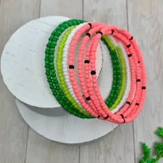 four bracelets are sitting on top of a white plate next to green and pink beads