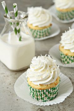 cupcakes with white frosting and sprinkles on plates next to a bottle of milk