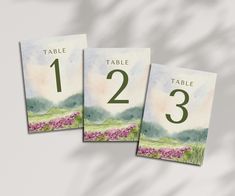 three place cards with watercolor flowers in the middle and numbers on each one side