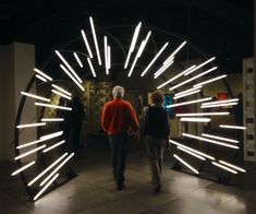 two people walking through an art exhibit with lights on the walls and in the ceiling