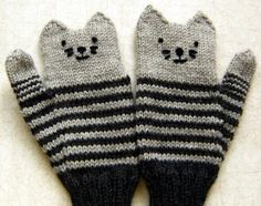 two gray and black knitted cats mittens with faces drawn on them, sitting on a white surface