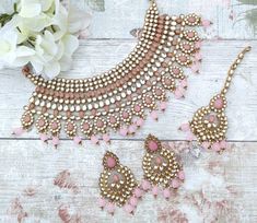 a pink necklace and matching earrings on a white wooden surface with flowers in the background