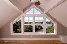 an empty room with a ceiling fan and large windows overlooking the water in the distance