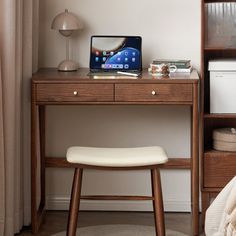 a laptop computer sitting on top of a wooden desk next to a white chair and bookshelf