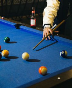 a man is playing pool with his cues and beer on the table in front of him