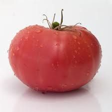 a tomato with water droplets on it sitting on a white surface, ready to be eaten